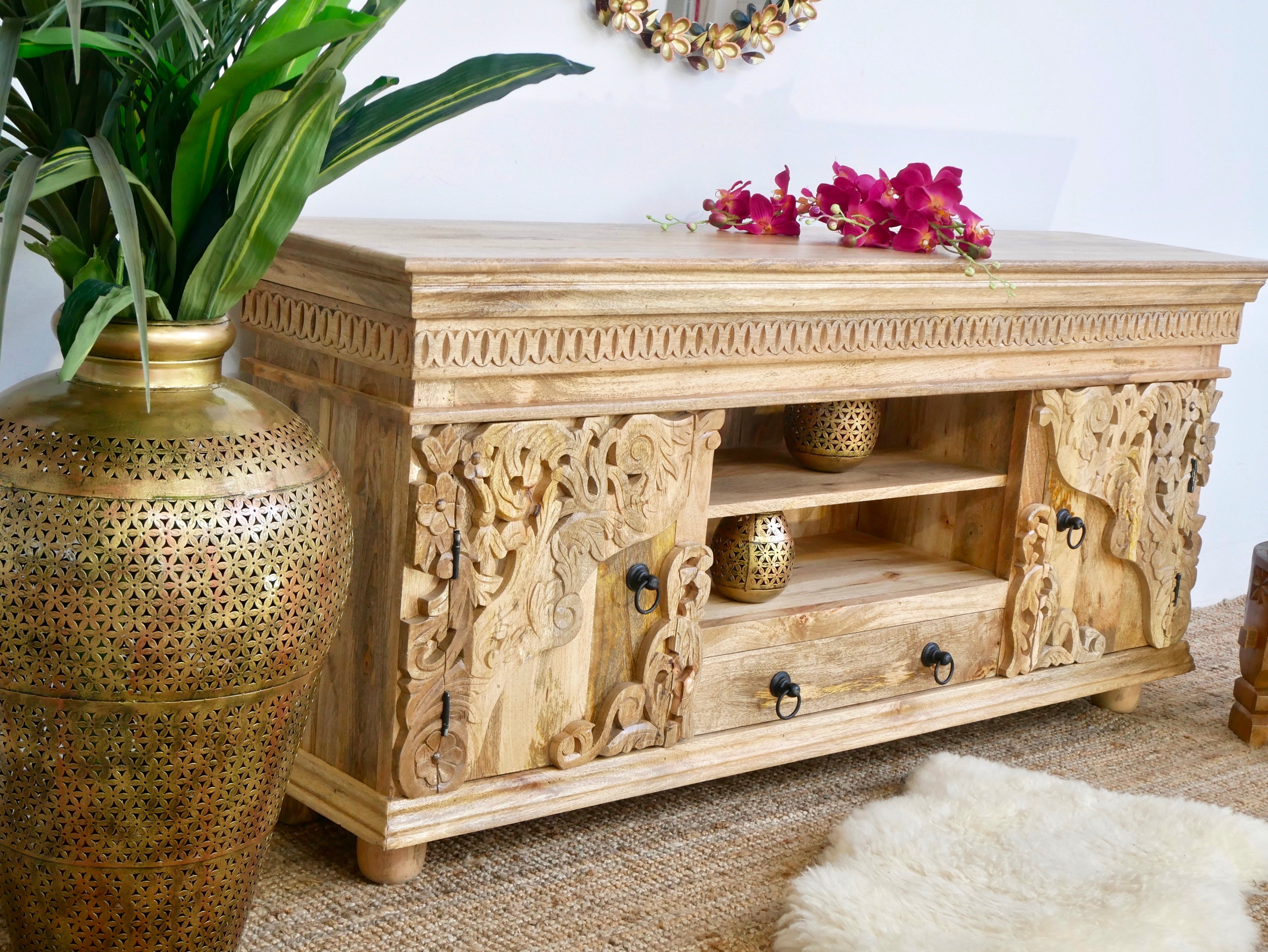 Side angle image of a hand-carved mango wood lowboard with two doors, one drawer, and open shelving; carved wooden sideboard for living or media room, 160 × 75 × 40 cm.