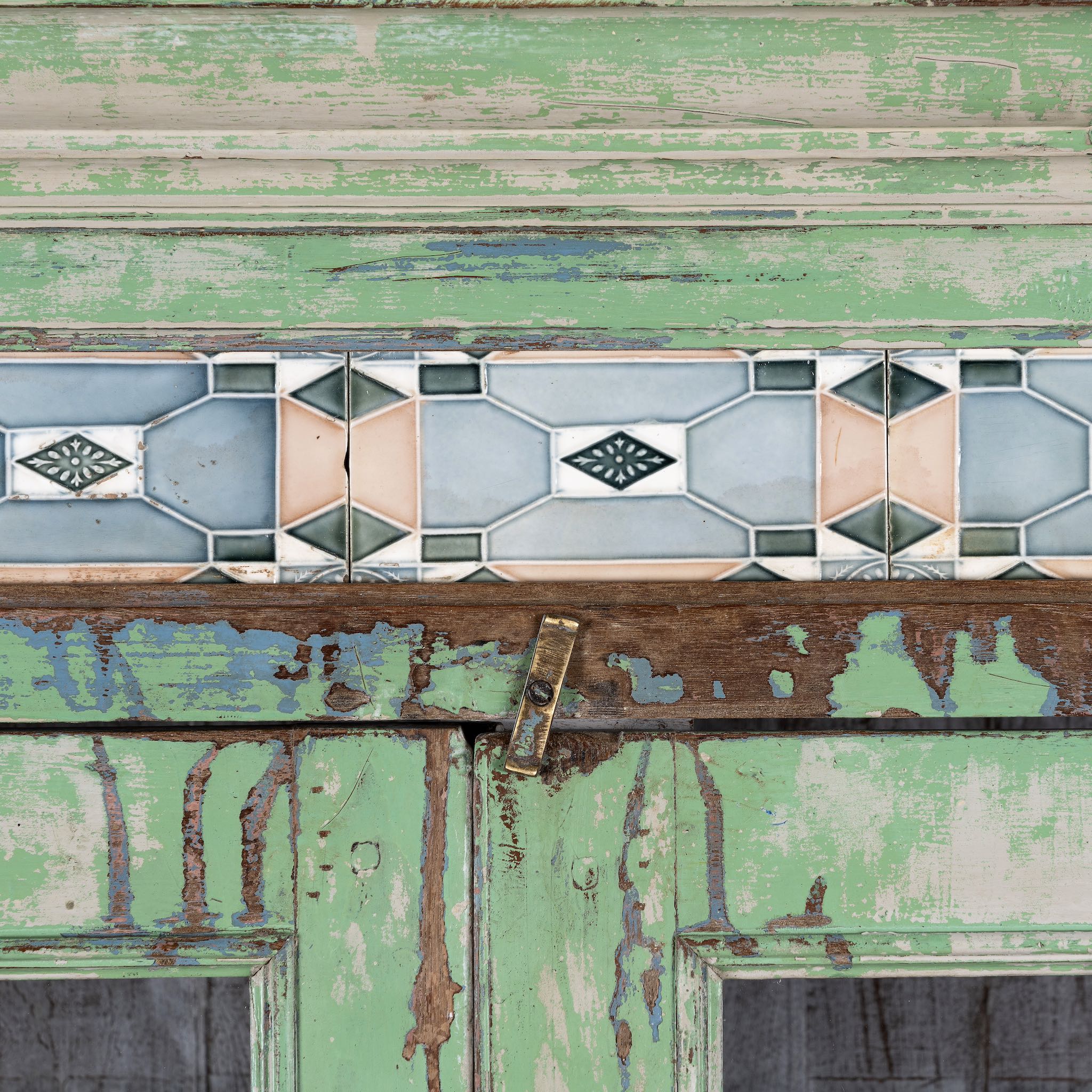 Close up image of a reclaimed teak wood vitrine with distressed green finish, ceramic inlays, and glass-panelled doors – sustainable furniture with vintage Indian charm.