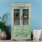 Reclaimed teak wood vitrine with distressed green finish, ceramic inlays, and glass-panelled doors – sustainable furniture with vintage Indian charm.