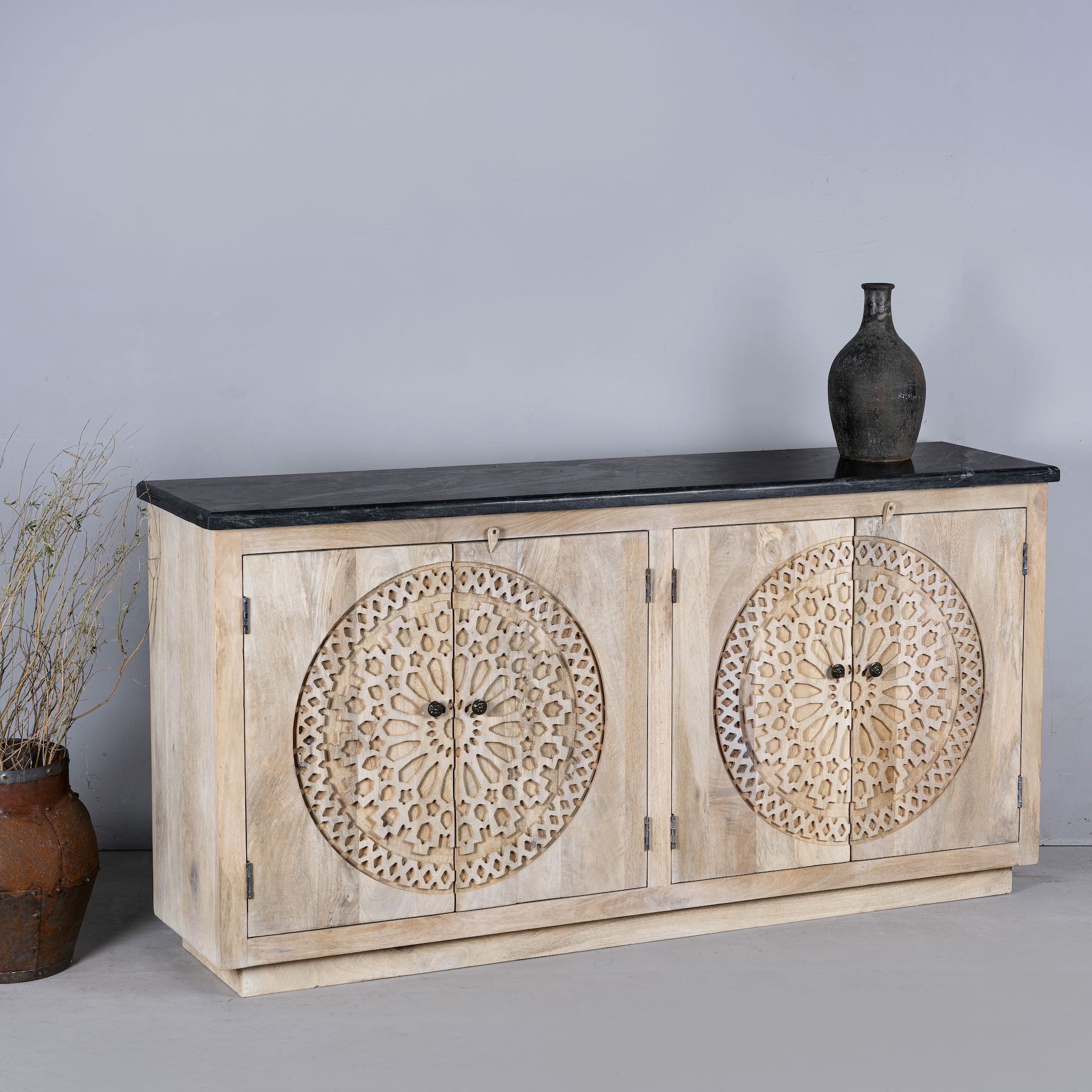 Side view of an acacia wood sideboard with 4 doors and iron fitted door knobs with floral round carvings and a black marble top.