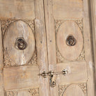 Close up image of a heavy reclaimed Indian teak door with unique hand carvings, sandblasted finish, and original brass hardware, extended to fit European height within a restored frame.