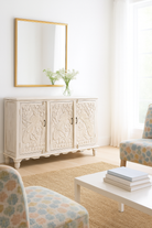 Lifestyle image of a hand-carved mango wood sideboard with peacock and foliage motifs, whitewashed finish; perfect for Indian home decor, 150 × 95 × 40 cm.