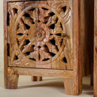 Close up picture f a pair of hand-carved bedside tables made of mango wood, featuring intricate round floral hand carvings on the doors. 