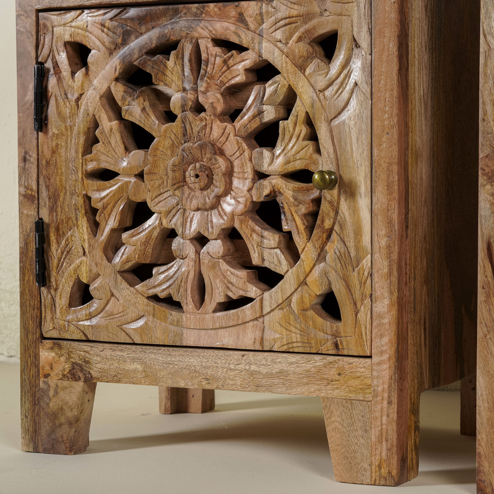 Close up picture f a pair of hand-carved bedside tables made of mango wood, featuring intricate round floral hand carvings on the doors. 