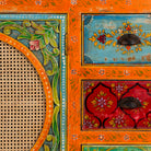 Close up image of a vintage style furniture sideboard with hand-painted floral motifs and rattan door inserts, bohemian rattan door furniture, 160 × 40 × 90 cm.