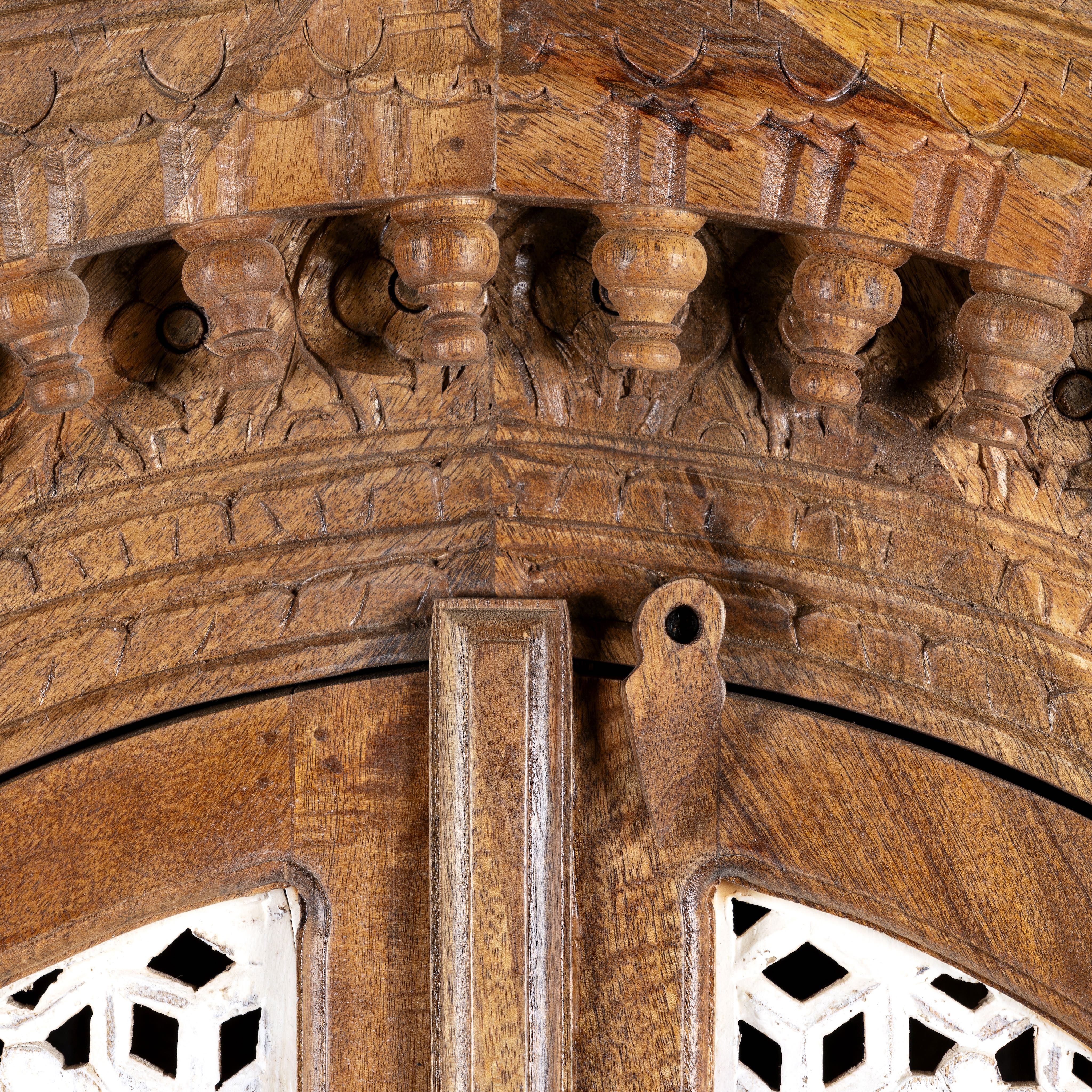 Close up image of a handcrafted carved wooden wardrobe in half-round design with whitewashed lattice panels – bedroom furniture with Mediterranean flair and artistic detail.