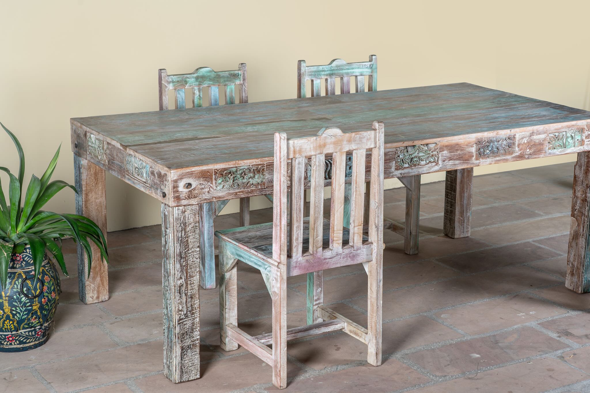 Side angle image of a reclaimed wood dining set Ayla with one vintage table and six rustic chairs. A handcrafted bohemian interior piece combining sustainable materials with artistic, timeworn charm.