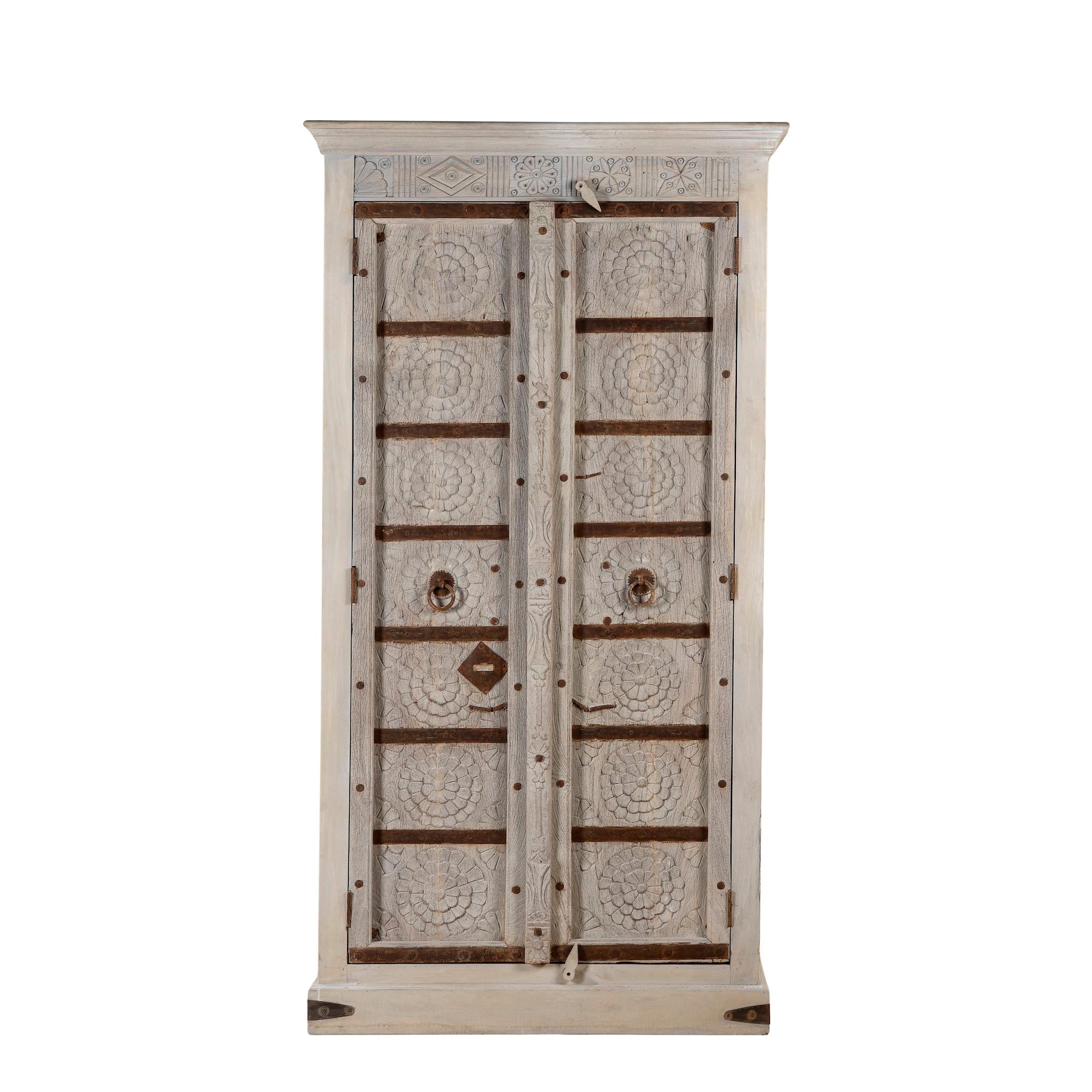 White background image of a handcrafted wooden wardrobe made from antique Indian teak doors with iron accents and floral carvings, combined with a solid mango wood body. A tall, rustic cabinet ideal for vintage-inspired or heritage-style interiors.