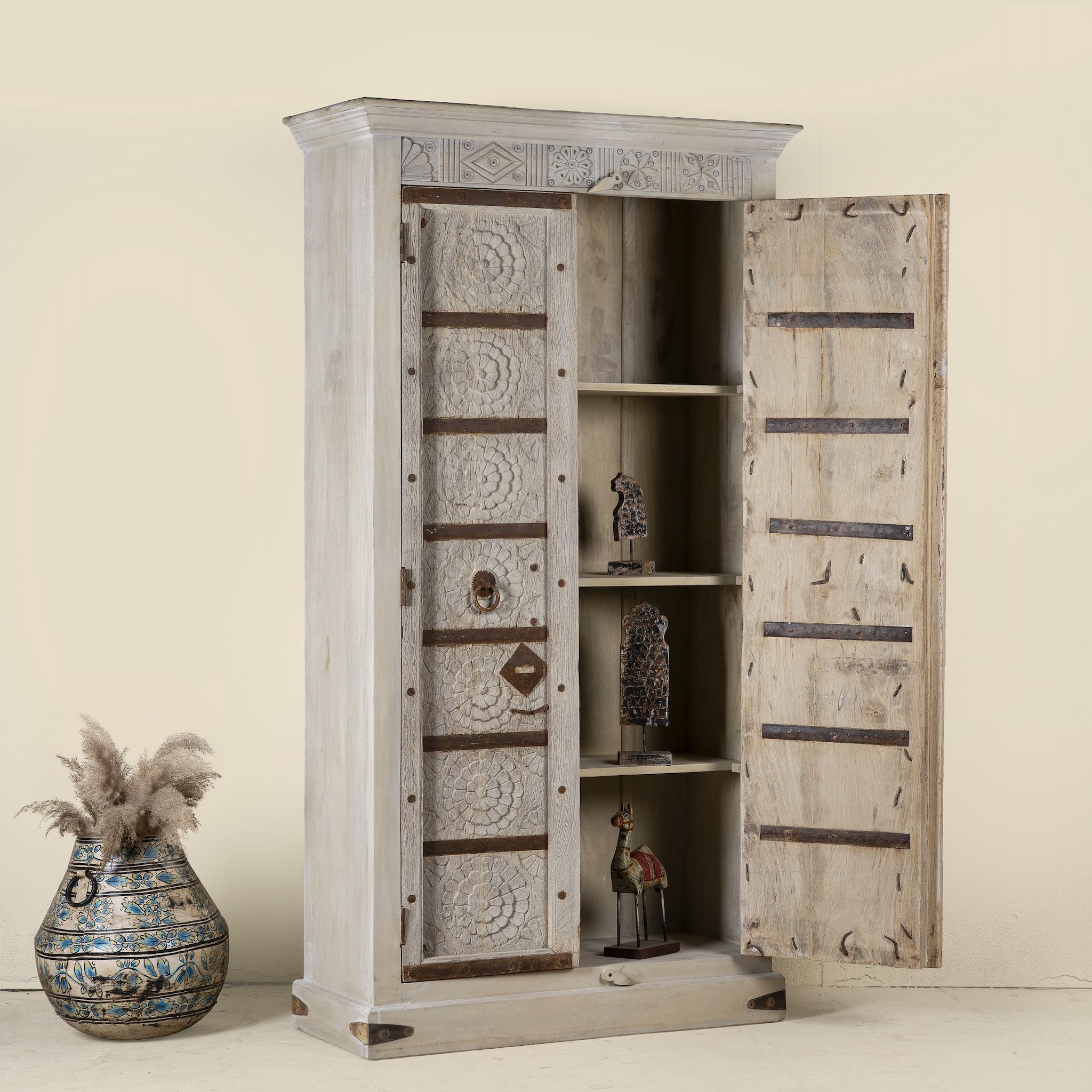 Open door image of a handcrafted wooden wardrobe made from antique Indian teak doors with iron accents and floral carvings, combined with a solid mango wood body. A tall, rustic cabinet ideal for vintage-inspired or heritage-style interiors.