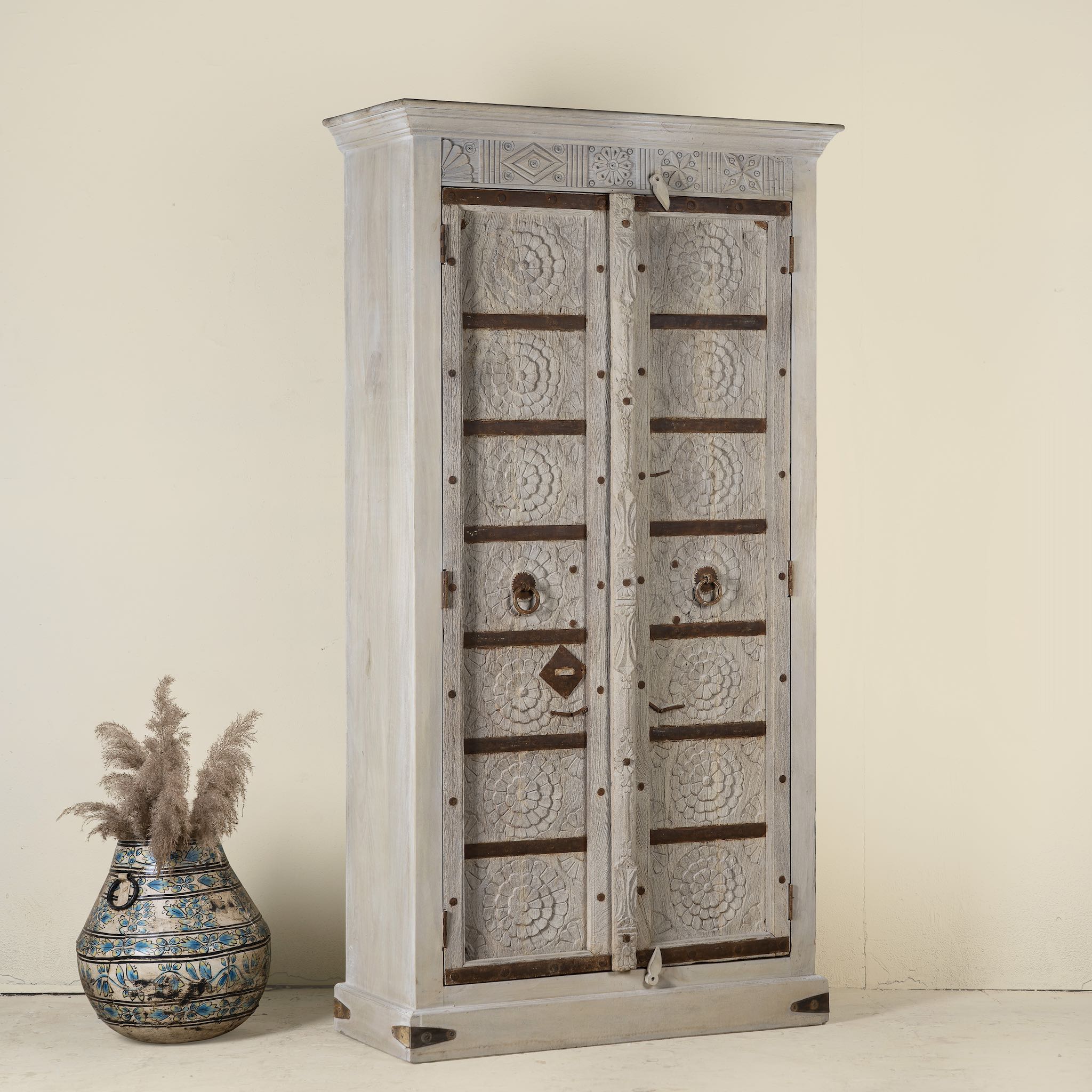 Side angle image of a handcrafted wooden wardrobe made from antique Indian teak doors with iron accents and floral carvings, combined with a solid mango wood body. A tall, rustic cabinet ideal for vintage-inspired or heritage-style interiors.