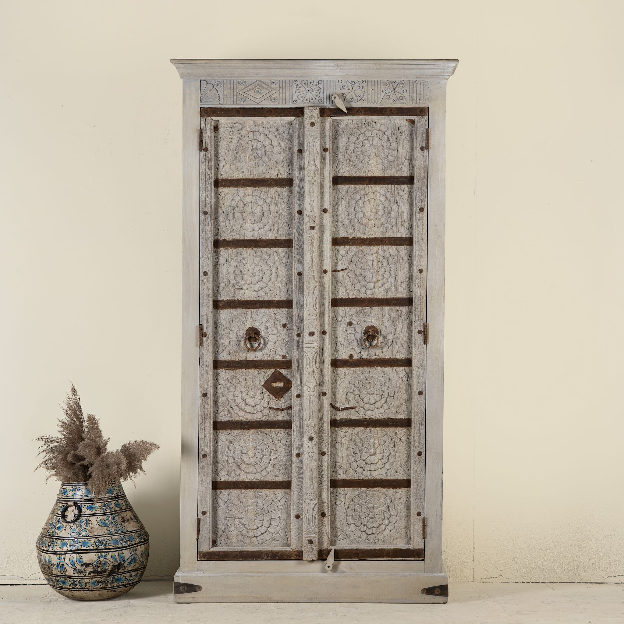 Handcrafted wooden wardrobe made from antique Indian teak doors with iron accents and floral carvings, combined with a solid mango wood body. A tall, rustic cabinet ideal for vintage-inspired or heritage-style interiors.