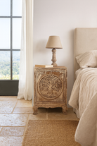 Lifestyle scene with a pair of mango wood bedside tables with hand-carved tree motifs and antique finish; perfect bedroom furniture and mango wood furniture, 50 × 70 × 40 cm.