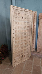 Bansuri hand-carved teak headboard made from an old Indian ceiling door, featuring grid-style floral carvings and a distressed whitewashed finish—an eye-catching piece of old door headboards and old Indian door furniture.