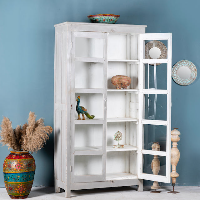 Side angle image with open door of a shabby chic teak wood cabinet with glass doors and five compartments – sustainable living room furniture crafted from refurbished old teak with rustic white finish.