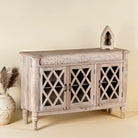 Side angle image of a rustic sideboard made of Mango wood with hand-carved details and glass panelled doors featuring a diamond lattice design.