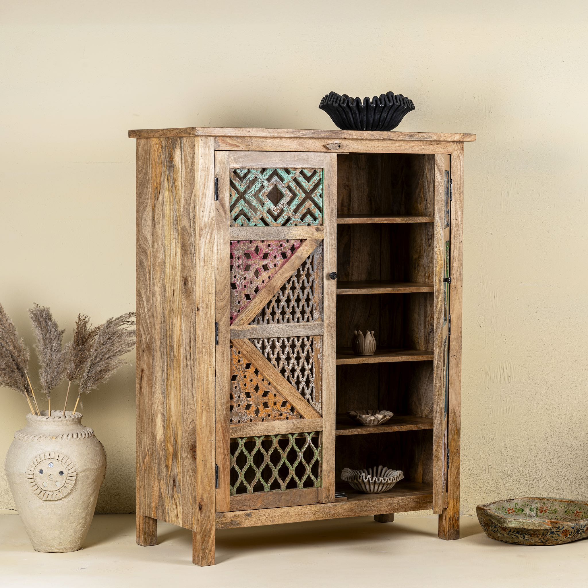 Side angle image with open door of a  handcrafted cabinet made from mango wood, featuring double doors with intricate multicoloured geometric latticework panels, combining natural wood tones with a vibrant, artisanal aesthetic.
