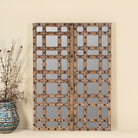 Statement wall mirror made from an old teak window frame with large square grid pattern, metal studs, and decorative center carving- a bold blend of rustic charm and historic craftsmanship.
