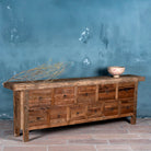 Side view image of a large wabi-sabi style console table crafted from reclaimed wood, featuring a natural weathered finish and multiple drawers with simple metal ring pulls, embracing rustic imperfection and minimalist charm.
