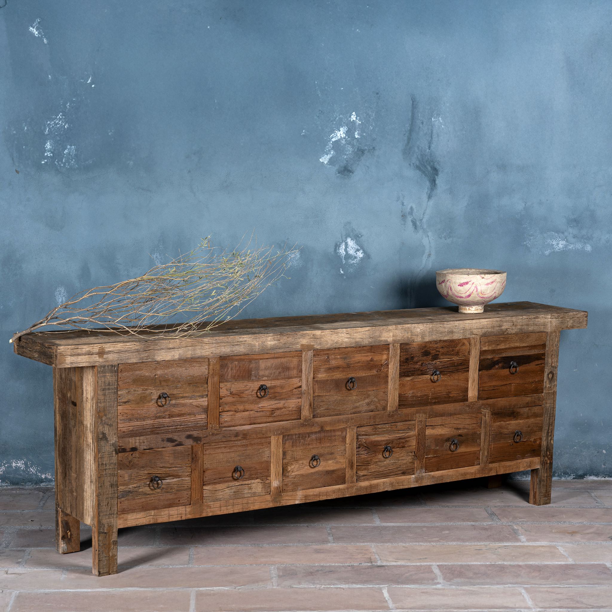 Side view image of a large wabi-sabi style console table crafted from reclaimed wood, featuring a natural weathered finish and multiple drawers with simple metal ring pulls, embracing rustic imperfection and minimalist charm.
