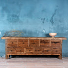 Front view image of a large wabi sabi style console table crafted from reclaimed wood, featuring a natural weathered finish and multiple drawers with simple metal ring pulls, embracing rustic imperfection and minimalist charm.
