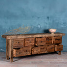 Side view image with open drawers of a large wabi-sabi style console table crafted from reclaimed wood, featuring a natural weathered finish and multiple drawers with simple metal ring pulls, embracing rustic imperfection and minimalist charm.
