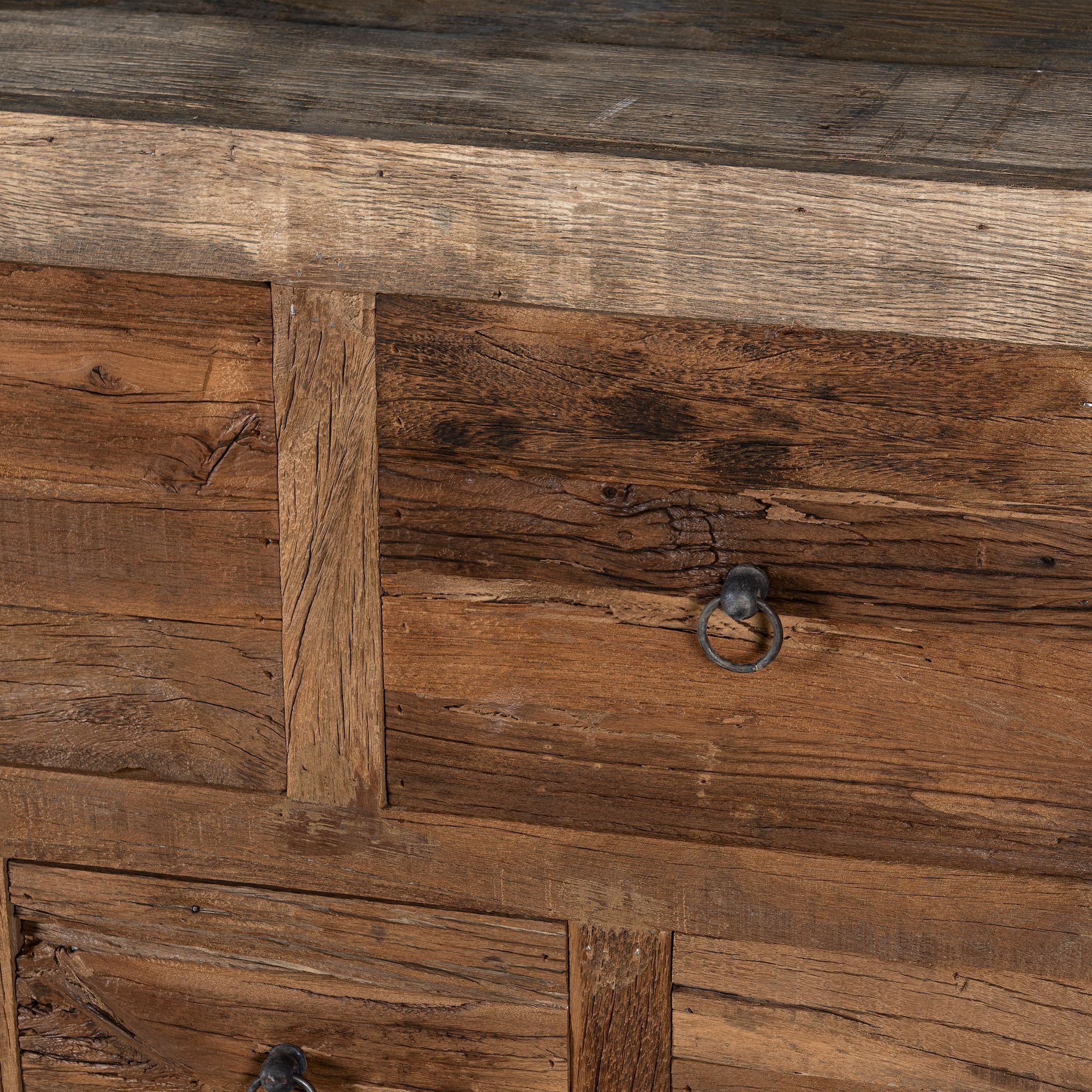Close up image of a large wabi-sabi style console table crafted from reclaimed wood, featuring a natural weathered finish and multiple drawers with simple metal ring pulls, embracing rustic imperfection and minimalist charm.
