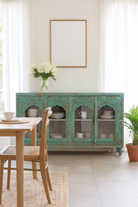 Lifestyle image of a Jesar handcrafted turquoise-washed carved wooden sideboard with Indian motifs and open compartments; ideal as living room furniture or carved showcase, 180 × 100 × 40 cm.