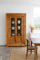 Lifestyle image of a hand carved display cabinet made from natural mango wood with floral detailing and glass-panelled doors; 180 × 110 × 40 cm.
