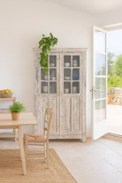 Lifestyle image of a refurbished antique teak wood display cabinet with whitewashed finish and glass doors – wooden display cabinet blending Mediterranean charm and timeless craftsmanship.