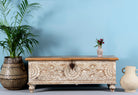 Hand-carved mango wood storage box with floral patterns and a natural wood top, accompanied by a vase with flowers and a pot with a plant.