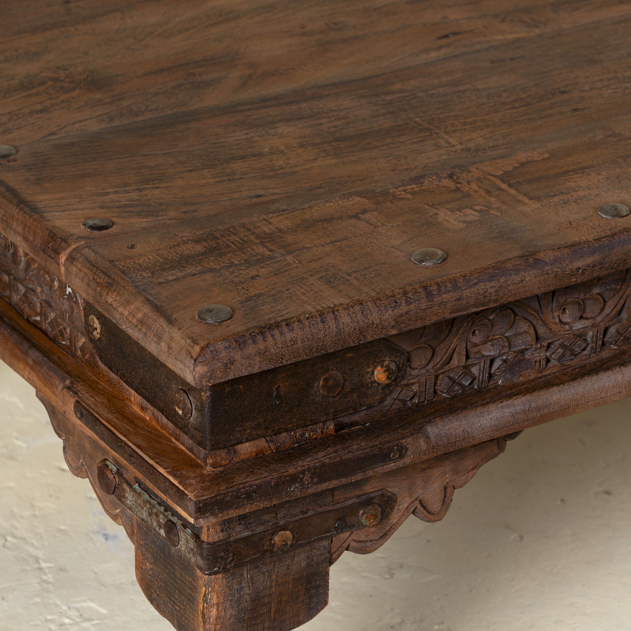 Close-up of a wooden table with intricate carvings and metal studs.