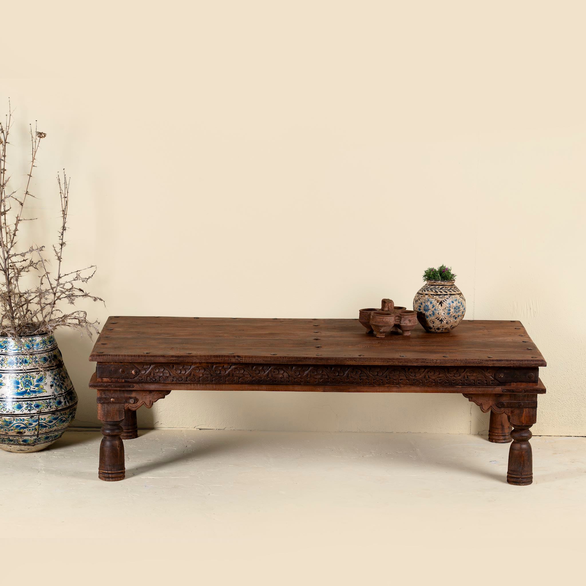 Lifestyle picture of a antique Indian coffee table crafted from solid teak wood, featuring detailed hand-carved floral motifs, traditional turned legs, and original iron fittings for an authentic heritage look.