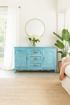 Lifestyle image of a hand-carved mango wood sideboard with distressed blue wash finish, artisanal furniture for bohemian interior, 150 × 40 × 90 cm.
