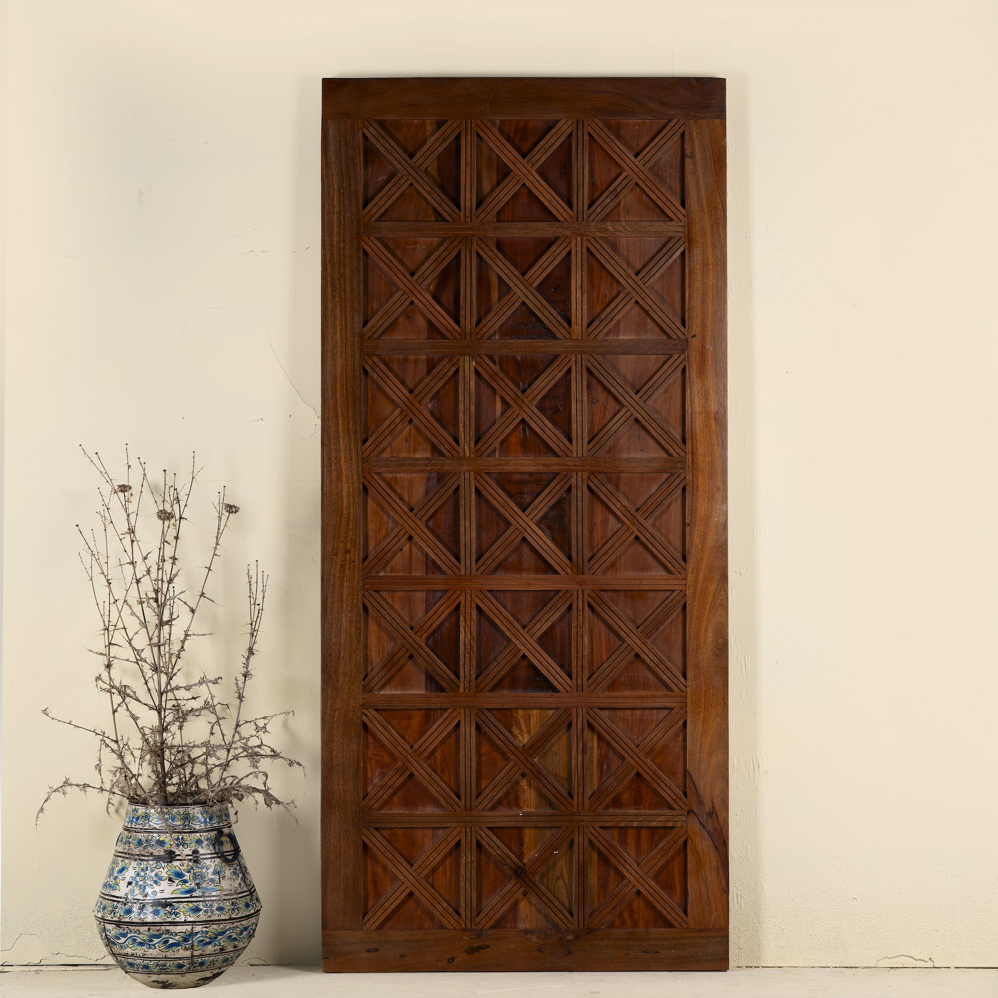 Decorative wooden panel with geometric pattern next to a vase with dried plants on a beige background