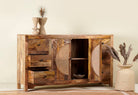 Open door image of a hand-carved mango wood sideboard with rattan inserts, featuring two cabinet doors with rattan fronts and six drawers, placed against a neutral backdrop with decorative items on top.