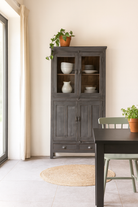 Lifestyle image of a shabby chic grey teak wood cabinet with glass doors and drawers – sustainable furniture for classic, rustic, or vintage interiors.