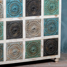 Close up view of a chest of 12 drawers made from mango wood, featuring hand-carved floral fronts in a mix of turquoise, black, and natural tones- a vibrant statement piece with vintage charm.