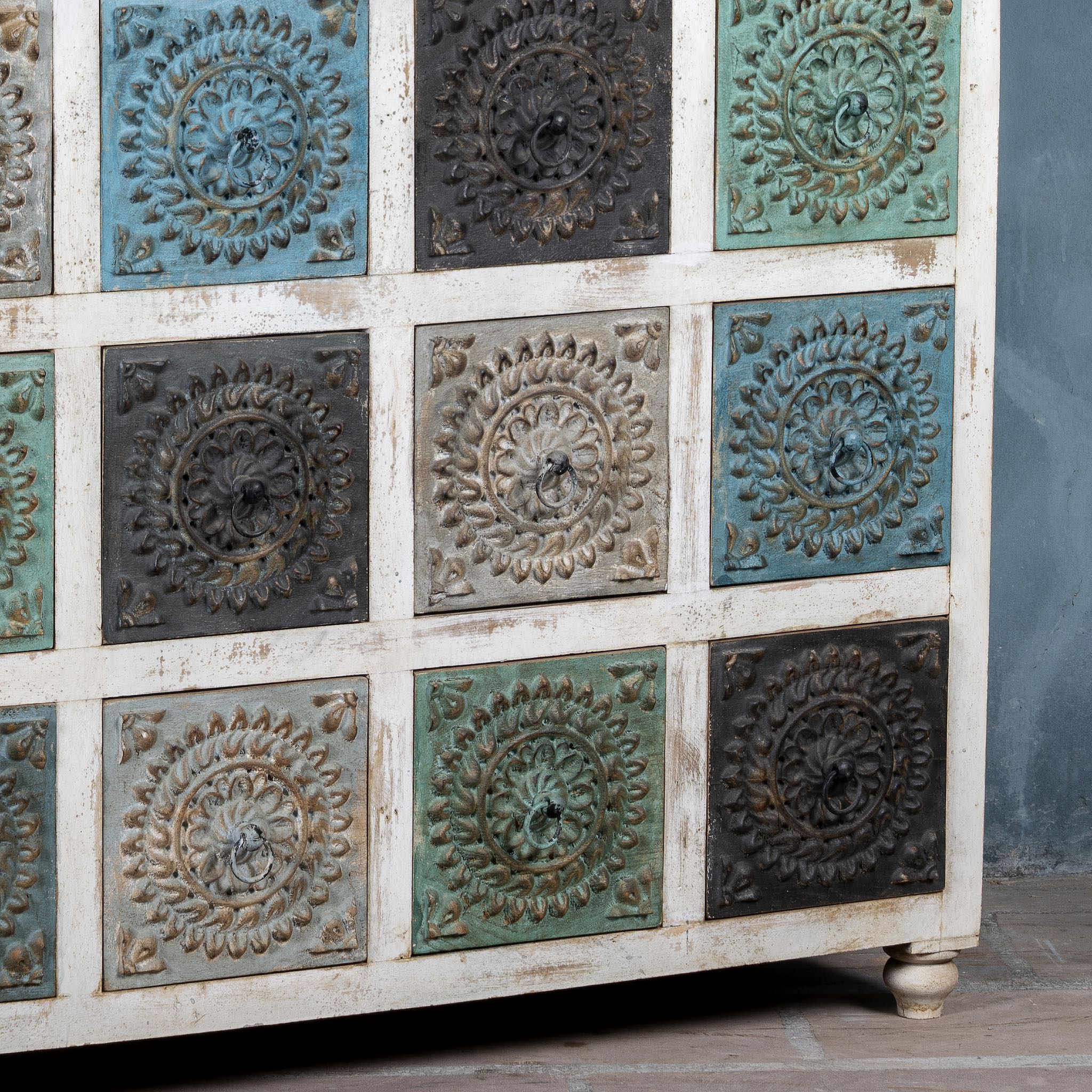 Close up view of a chest of 12 drawers made from mango wood, featuring hand-carved floral fronts in a mix of turquoise, black, and natural tones- a vibrant statement piece with vintage charm.