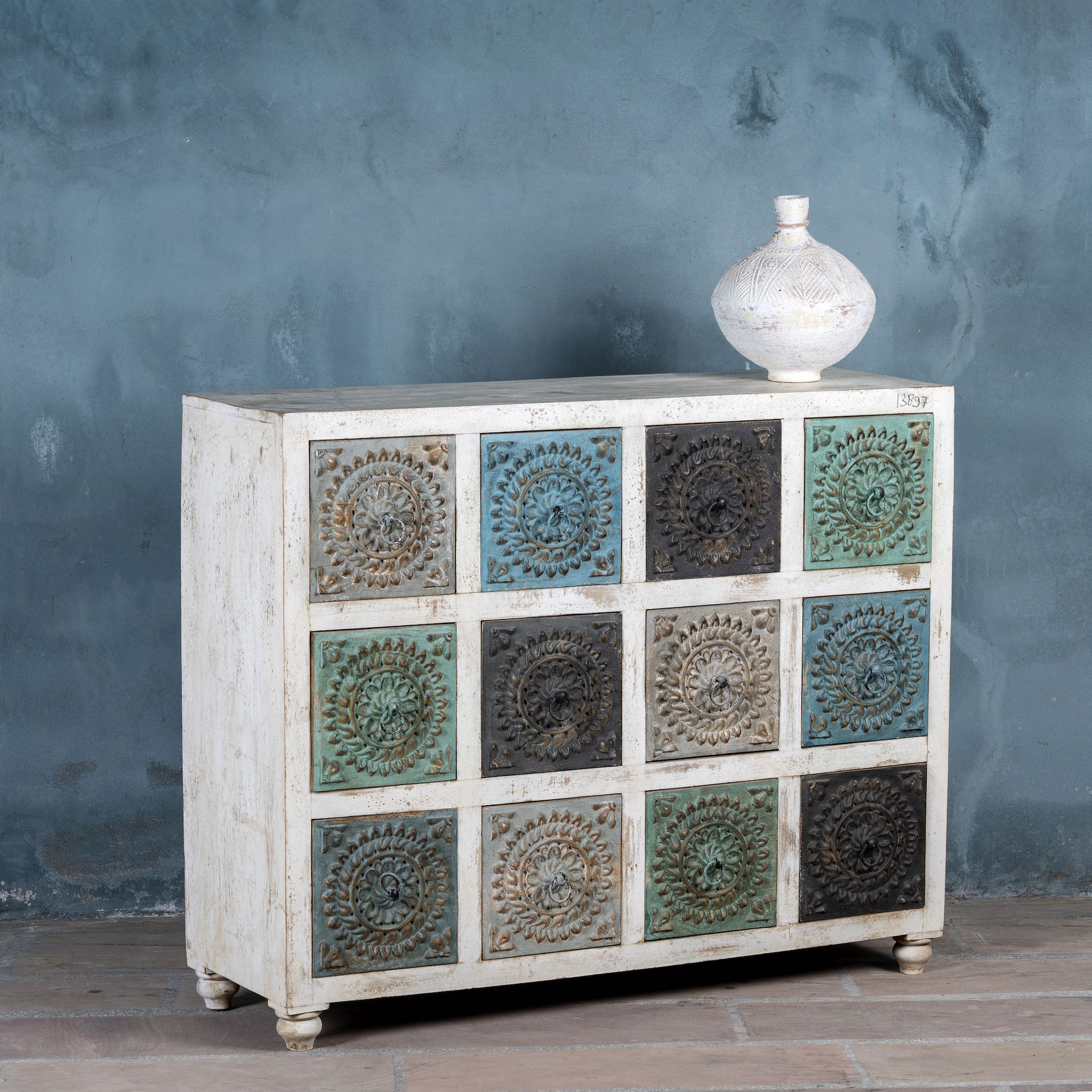 Side angle view of a chest of 12 drawers made from mango wood, featuring hand-carved floral fronts in a mix of turquoise, black, and natural tones- a vibrant statement piece with vintage charm.