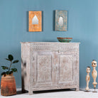 Side angle image of a grey-washed reclaimed wood cabinet with hand-carved floral and sunburst detailing, a vintage furniture piece perfect for rustic or bohemian interiors.