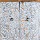 Close up image of a hand-carved mango wood cupboard Utkarsh with whitewashed doors featuring palm tree and botanical motifs. A Mediterranean-inspired piece of Indian furniture combining artisan detail with practical storage.
