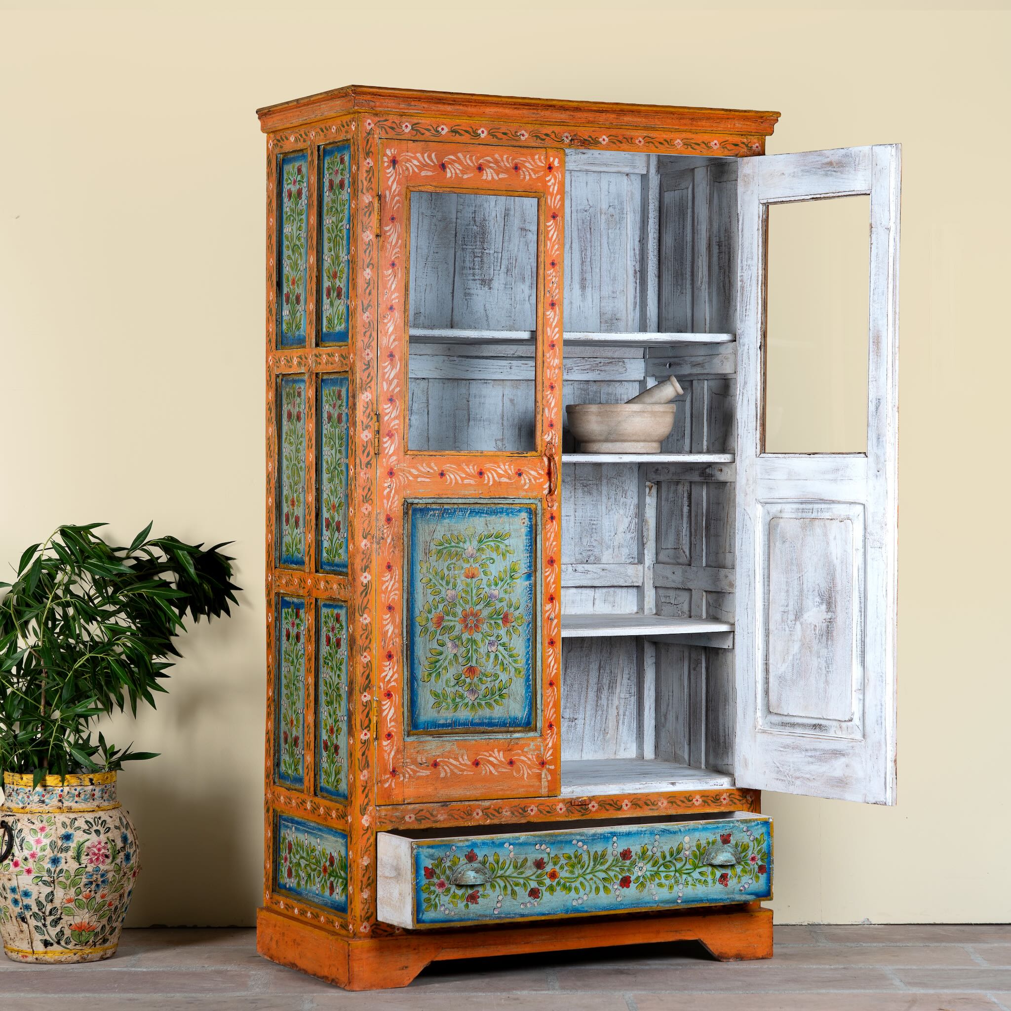Side angle with open doors of a hand-painted teak wood showcase with floral motifs and glass doors – sustainable furniture crafted from recycled wood with traditional Indian artistry.