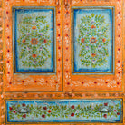 Close up image of a white background image of a hand-painted teak wood showcase with floral motifs and glass doors – sustainable furniture crafted from recycled wood with traditional Indian artistry.