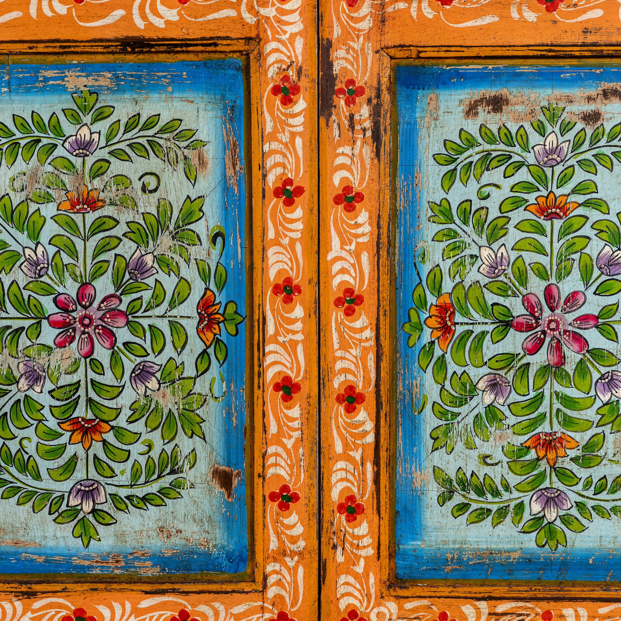 Close up image of a hand-painted teak wood showcase with floral motifs and glass doors – sustainable furniture crafted from recycled wood with traditional Indian artistry.