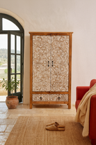 Life style image of a hand-carved mango wood wardrobe with whitewashed floral motifs – Zashil by Om Home & Garden, a Mediterranean-inspired piece of carved wooden furniture.
