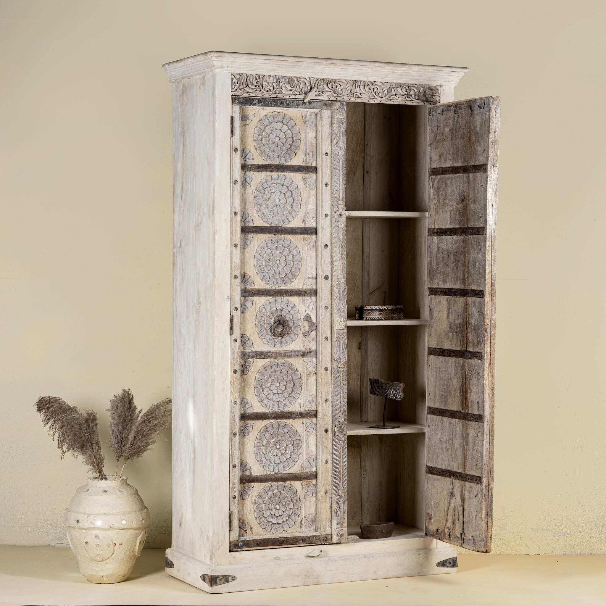 Open door view of a old teak door wardrobe with floral carvings and original iron fittings.