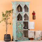 Side angle image with open doors of a hand-carved mango wood shelf with arched open display and lower cabinets – vintage home decoration piece in distressed pastel blue finish with Indian architectural detailing.
