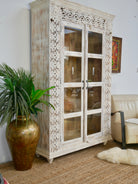 Side angle image of a handcrafted mango wood cabinet with glass-panelled doors and internal storage – carved wood furniture made from sustainable mango wood with unique natural grain.